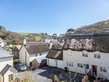 A group of houses with thatched roofs and garages in a rural area with hills in the background at Goody in Hope Cove