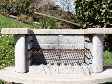 An outdoor stone barbecue grill with a metal grate in a garden