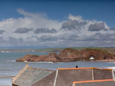 A coastal view with rocky cliffs ocean waves and rooftops at Goody in Hope Cove