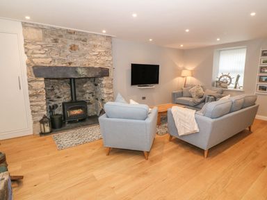 A living room with light blue sofas a wooden floor and a stone fireplace at Fishermans Cottage in Malltraeth