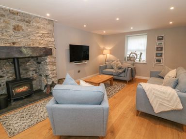 A living room with blue sofas a stone fireplace a wall-mounted TV and a wooden coffee table at Fishermans Cottage in Malltraeth