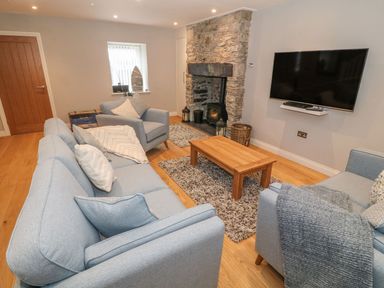A living room with blue sofas a wooden coffee table a stone fireplace and a wall mounted TV at Fishermans Cottage in Malltraeth
