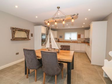 A kitchen with white cabinets a wooden table four chairs and a model sailboat at Fishermans Cottage in Malltraeth