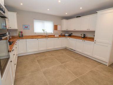 A kitchen with white cabinets wooden countertops and large tile flooring at Fishermans Cottage in Malltraeth