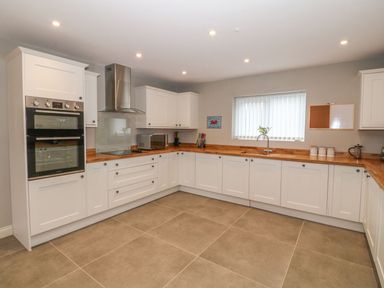 A kitchen with white cabinets wooden countertops a double oven stove microwave and a window at Fishermans Cottage in Malltraeth