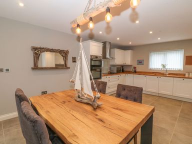 A kitchen with white cabinets wooden countertops a wooden dining table with a sailboat model and upholstered chairs at Fishermans Cottage in Malltraeth