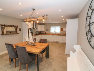 A kitchen with white cabinets a wooden dining table with four chairs and a decorative sailboat at Fishermans Cottage in Malltraeth
