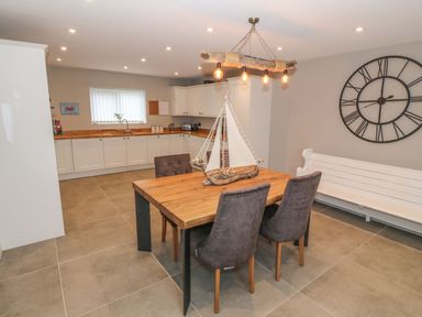 A kitchen with a wooden dining table and chairs a large wall clock and a bench at Fishermans Cottage in Malltraeth