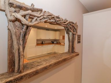 A kitchen with cream cabinets and wooden countertops seen through a window frame made of rustic branches at Fishermans Cottage in Malltraeth