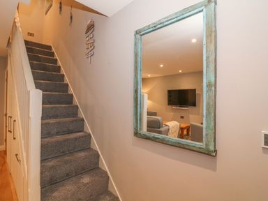 A carpeted staircase with white railing and a wall mirror reflecting a living room at Fishermans Cottage in Malltraeth