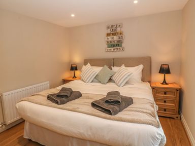 A bedroom with a double bed flanked by wooden bedside tables each with a lamp and a sign above the bed at Fishermans Cottage in Malltraeth