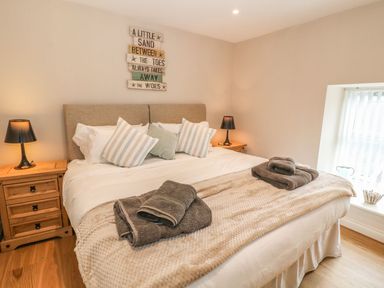 A bedroom with a bed with pillows and folded towels on a blanket bedside tables with lamps and a window at Fishermans Cottage in Malltraeth