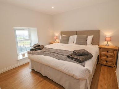 A bedroom with a bed pillows bedside tables lamps and a window at Fishermans Cottage in Malltraeth