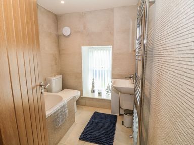 A bathroom with a bathtub toilet sink window with decorations and a blue floor mat at Fishermans Cottage in Malltraeth
