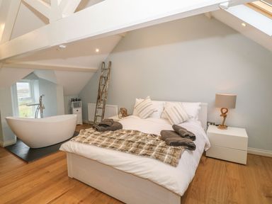 A bedroom with a double bed a freestanding bathtub and wooden ladder at Fishermans Cottage in Malltraeth