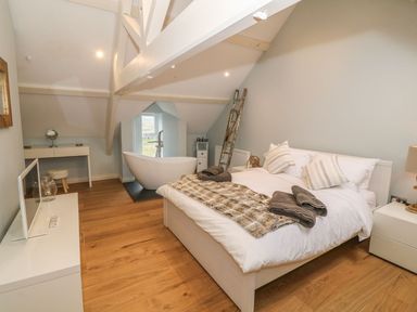 A bedroom with a bed beside a freestanding bathtub and a TV on a cabinet at Fishermans Cottage in Malltraeth