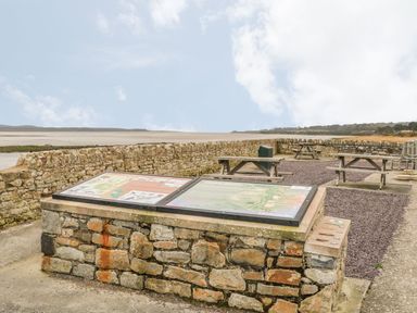 A stone information board with picnic tables and a stone wall near a beach at Fishermans Cottage in Malltraeth