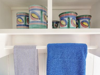 A white shelf with colorful ceramic pots on the top and two towels hanging below one striped and one blue at Shepherds Hut Boconnoc near Lostwithiel