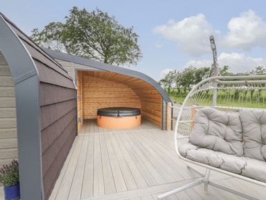 An outdoor deck area with a covered hot tub and a cushioned hanging chair at Laird Lodge 5 Lochmaben