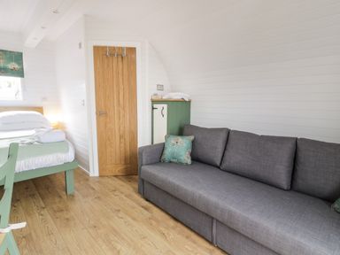 A room with a gray sofa wooden floor a bed with white bedding and a wooden door at Laird Lodge 5 in Lochmaben