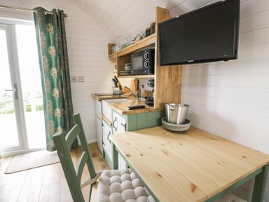 A small kitchen area with wooden countertop green cabinets a table with a chair and a wall mounted television at Laird Lodge 5 Lochmaben