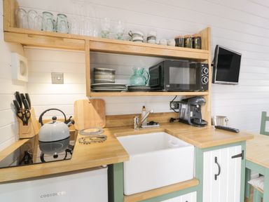 A kitchen corner with a white sink wooden countertops a microwave glassware and dishes at Laird Lodge 5 in Lochmaben