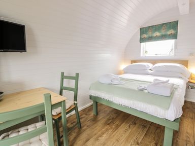 A bedroom with a double bed, a small table with two chairs, a wall-mounted TV, and a window with a green patterned blind at Laird Lodge 5 in Lochmaben