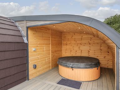 A covered outdoor wooden space with a round hot tub and a small mat in front at Laird Lodge 5 in Lochmaben