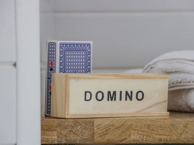 A box labeled domino next to a deck of playing cards and folded towels on a wooden surface at Laird Lodge 5 in Lochmaben