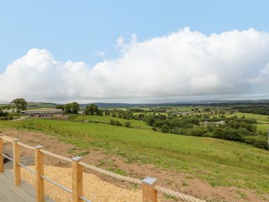 A rural landscape with green fields trees and farm buildings viewed from a wooden deck at Laird Lodge 5 in Lochmaben