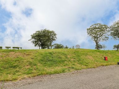 An outdoor scene with a grassy hill, trees, a gravel path, and a red object on the right at Laird Lodge 5 in Lochmaben