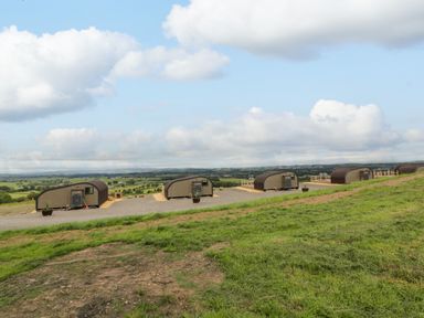 A row of small wooden cabins on a grassy hillside with a view of the countryside at Laird Lodge 5 in Lochmaben