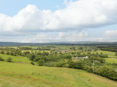 A rural landscape with green fields trees and scattered buildings under a partly cloudy sky at Laird Lodge 5 Lochmaben