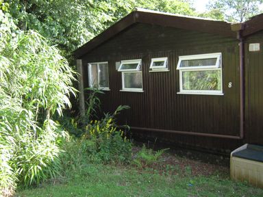 A dark brown building with four windows and plants in front at 8 The Park in Kilkhampton