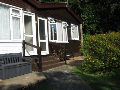 The exterior of a brown and white house with white doors and windows a bench and a bush in the garden at 8 The Park in Kilkhampton