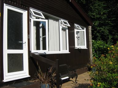 Exterior of a dark brown building with white framed doors and windows and a small garden with flowers at 8 The Park in Kilkhampton