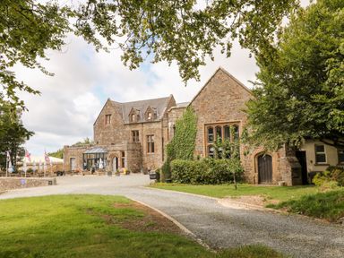 A stone building with outdoor seating umbrellas and a gravel driveway at 8 The Park in Kilkhampton