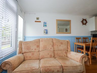 A living room with a beige sofa wooden dining table and chairs a wall mirror and a ship wheel clock at 8 The Park Kilkhampton