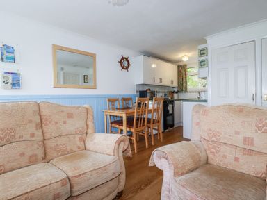 A sitting area with two beige sofas and a dining area with a wooden table and four chairs next to a kitchen at 8 The Park in Kilkhampton