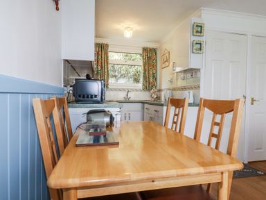 A kitchen dining area with a wooden table and chairs and kitchen appliances at 8 The Park in Kilkhampton