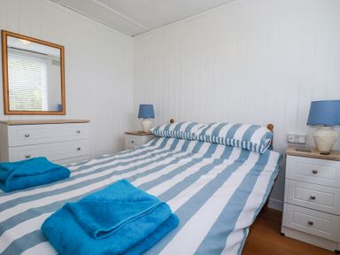 A bedroom with a striped bed linen two blue towels on the bed bedside tables with lamps and a dresser with a mirror at 8 The Park in Kilkhampton