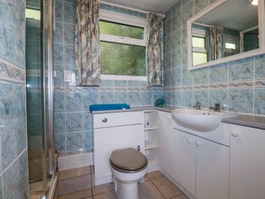 A bathroom with a toilet and sink with storage cabinets and a window with curtains at 8 The Park in Kilkhampton