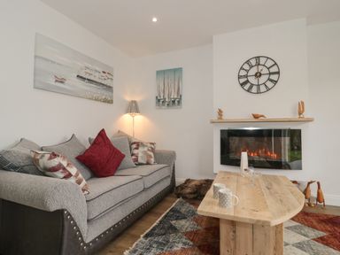 A living room with a grey sofa with cushions a wooden coffee table a wall clock and an electric fireplace at The Hideaway in Lympsham near Brean
