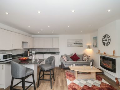 An open plan kitchen and living area with grey chairs, a grey sofa, a wooden coffee table, and a fireplace at The Hideaway in Lympsham near Brean