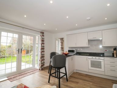 A kitchen with white cabinets black countertop a stove microwave two chairs and glass doors leading to a garden at The Hideaway in Lympsham near Brean