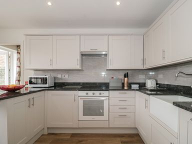 A kitchen with white cabinets a black countertop microwave oven sink and knife holder at The Hideaway in Lympsham near Brean