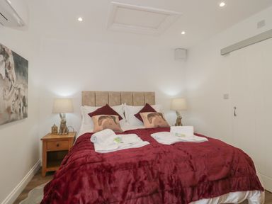 A bedroom with a double bed covered with a red blanket and pillows two bedside tables with lamps and rabbit figurines at The Hideaway in Lympsham near Brean