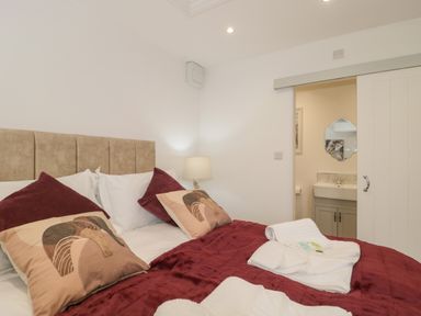 A bedroom with a bed covered with a red blanket and pillows next to a lamp and a sliding door leading to a bathroom at The Hideaway in Lympsham near Brean