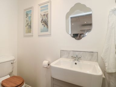A bathroom with a toilet with a wooden seat a white sink with a mirror above and two framed pictures on the wall at The Hideaway in Lympsham near Brean