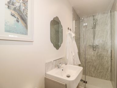 A bathroom with a sink a mirror two white robes hanging and a glass shower enclosure at The Hideaway in Lympsham near Brean